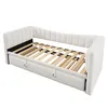 A white upholstered daybed with a wooden slat mattress support and a pull-out trundle bed underneath, shown from a diagonal angle against a white background. Anteprima dell’immagine prodotto