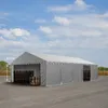 A large grey tent structure is set up outdoors on a paved surface, with stacks of wooden pallets visible inside and near the entrance. The sky above is blue with scattered white clouds. Produktbild-Vorschau