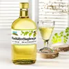 A bottle of liqueur and a glass of the same liqueur are displayed on a table with decorative wooden coasters and greenery in the background. Produktbild-Vorschau
