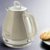 A vintage-style electric kettle is shown on a surface with a plate of cookies in the background. Anteprima dell’immagine prodotto