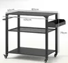 A black metal grill cart with three shelves and a side basket, shown with dimensions indicated by text overlays. Produktbild-Vorschau