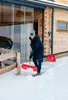 A man is shoveling snow in front of a wooden house with large glass doors. Náhled obrázku produktu