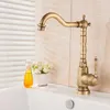 A close-up shot of a vintage-style brass faucet on a white sink, with a small bottle of yellow liquid and a pot of white flowers in the background. Náhled obrázku produktu
