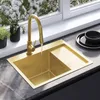 A modern kitchen sink with a gold faucet and a gold sink basin, set against a window with white flowers outside and black dishes on the counter. Náhľad obrázku produktu
