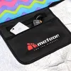 A close-up view of a black zippered pocket on a picnic blanket, showing a smartphone and keys inside. Produktbild-Vorschau