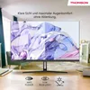 A monitor is displayed in a living room setting, with text overlays highlighting its features. Produktbild-Vorschau