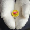 Hands wearing white knitted gloves holding a small round tin of Carmex lip balm. Anteprima dell’immagine prodotto