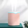 A pink humidifier with two streams of mist emitting from the top, placed on a teal surface against a light gray wall. Náhled obrázku produktu