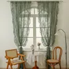 A room interior with a window dressed with green lace curtains, a small round table with a figurine and a teacup, and two chairs. Produktbild-Vorschau