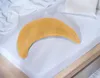 A crescent-shaped pillow with a yellow-orange cover lies on a white bedsheet. Produktbild-Vorschau