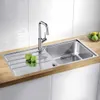 A stainless steel kitchen sink with a drainboard and faucet, with two green apples on the drainboard and a bowl of fruit in the background. Anteprima dell’immagine prodotto