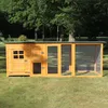 A wooden chicken coop with an attached run is set up on a grassy lawn with trees in the background. Produktbild-Vorschau