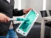 A person is holding a mop head and handle in a room with a table and chairs. Produktbild-Vorschau