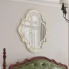 A decorative mirror hangs on a wall above a tufted headboard. Produktbild-Vorschau