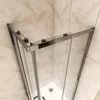 A top-down view of a shower cabin with glass doors and silver metal frames, set against a tiled wall. Produktbild-Vorschau