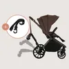 A brown stroller with a black strap accessory shown with a plus sign, indicating it is an add-on. Náhľad obrázku produktu