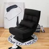 A dark gray floor chair with a lumbar pillow sits on a round rug with alphabet letters printed on it. A large abstract painting is in the background, and a stack of books is to the right of the chair. Produktbild-Vorschau