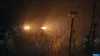 A dark, foggy scene with car headlights illuminating tall grass and a shovel. Produktbild-Vorschau