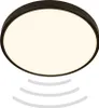 A close-up studio shot of a round, black-rimmed LED ceiling light with a white diffuser, emitting a warm white light. Below the light, three curved, light gray lines suggest motion or sensor waves. Voir les images du produit