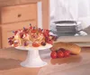 A food display with a cake stand filled with appetizers, bread, and tomatoes on a wooden table. Produktbild-Vorschau