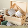 A wooden box filled with spools of twine and burlap, placed on a patterned blanket. Produktbild-Vorschau