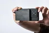 Hands holding a smartphone with a carbon fiber textured case and a camera module. Produktbild-Vorschau