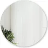 A round mirror reflecting a room with sheer white curtains and a plant. Náhled obrázku produktu