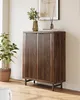 A dark wood cabinet with slatted doors stands in a room with a plant and artwork. Náhľad obrázku produktu