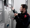 An electrician is working on an electrical panel with a cordless drill and screwdriver. Anteprima dell’immagine prodotto