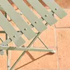 A close-up view of a folding bistro table and chairs set made of metal, set on a brick patio. Produktbild-Vorschau
