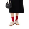 A person wearing sneakers and red socks, holding a black handbag. Produktbild-Vorschau