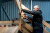 A man is using a cordless drill to assemble a wooden structure, possibly stairs or a platform. Tools and hardware are visible on a wooden surface. Anteprima dell’immagine prodotto