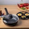 A frying pan with a lid and an egg insert, along with some food items, are arranged on a wooden table. Voir les images du produit