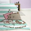 A blanket with a Pusheen cat design is spread on a bed, with a pizza box, donut, and game controller nearby. Produktbild-Vorschau