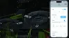 A close-up of a robotic lawnmower's cutting blades with a smartphone displaying its control app. Voir les images du produit