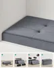 A grey upholstered storage ottoman in a corner, with inset images showing assembly steps. Náhled obrázku produktu