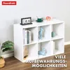 A white cube shelf unit is displayed with decorative items and books on its shelves, set against a light gray wall and wooden floor. Náhled obrázku produktu
