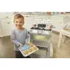 A young boy is standing in a kitchen-like setting, holding a tray of toy food in front of a toy oven. Anteprima dell’immagine prodotto