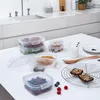 A collection of clear plastic food storage containers filled with berries, cookies, and granola, arranged on a white table with a kitchen counter in the background. Produktbild-Vorschau