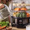 A person is pouring water into a food steamer that is filled with food. Náhled obrázku produktu