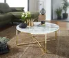A living room scene featuring a round marble-look coffee table with a gold metal frame, placed on a patterned rug in front of a green sectional sofa. Decorative items like a teapot and vase with flowers are on the table. Anteprima dell’immagine prodotto