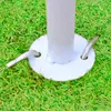 A close-up view of the base of a white pole, anchored to the ground with a white circular plate and two metal pins, set against a backdrop of green artificial grass. Anteprima dell’immagine prodotto