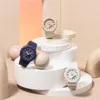 Three Casio G-Shock watches are displayed on white geometric stands, with soft pastel-colored spheres and a gradient background. Podgląd zdjęcia produktu