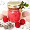 A jar of raspberry chia seed jam with raspberries and chia seeds around it. Produktbild-Vorschau