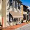 A retractable awning is installed on the side of a row of houses on a street. Produktbild-Vorschau