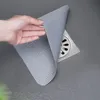 A hand is holding a gray silicone drain cover over a square shower drain. Produktbild-Vorschau