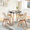 A dining set with a round black table and four white chairs with gray cushions, placed on a patterned rug in a room with a window and wall art. Voir les images du produit