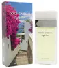 Parfumflakon Dolce & Gabbana Light Blue Escape to Panarea neben Verpackung mit mediterraner Küstenlandschaft, Palmen und pinken Bougainvilleen. Podgląd zdjęcia produktu