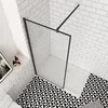 A modern bathroom with a walk-in shower, black framed glass, white subway tile walls, and a black and white geometric floor. Produktbild-Vorschau