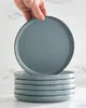 A hand is holding up a blue plate, with a stack of similar plates below it, on a marble-like surface. Produktbild-Vorschau